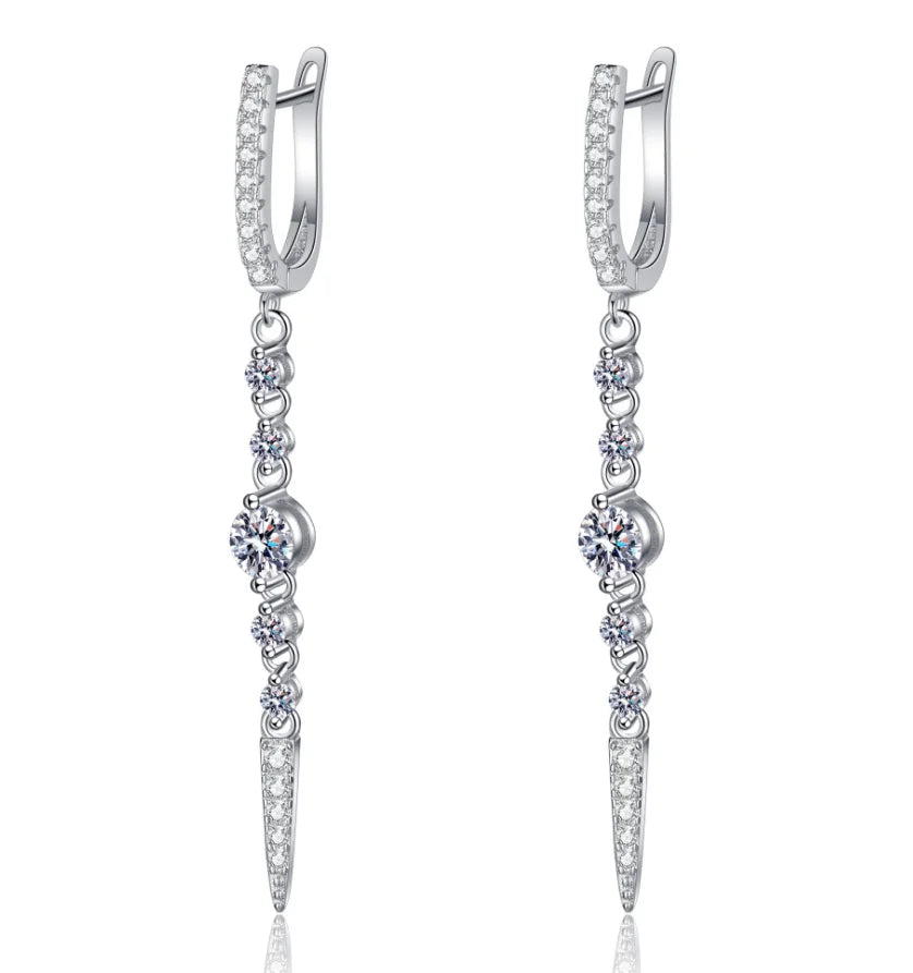 A pair of silver huggie hoop earrings with dangling chains of clear cubic zirconia stones, featuring a central round-cut clear stone and a pointed drop at the bottom, shown on a white background.