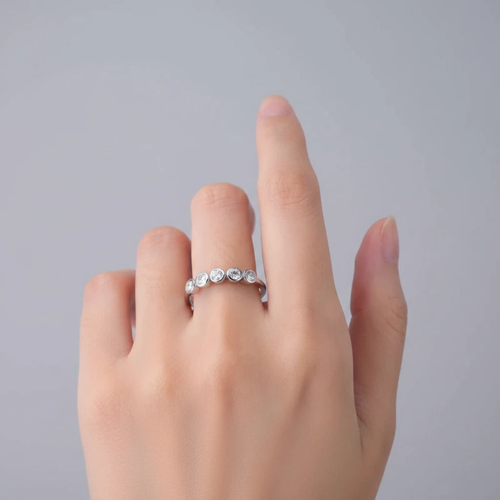 Hand wearing a silver ring with small stones on a light background
