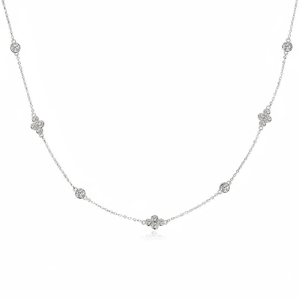 A delicate silver chain necklace featuring five small floral clover motifs and three round bezel-set clear stones spaced along the chain, displayed on a clean white background.