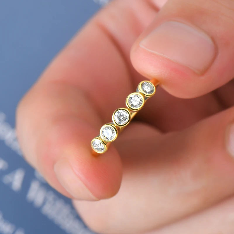Gold earring with clear stones held between fingers against a blurred background