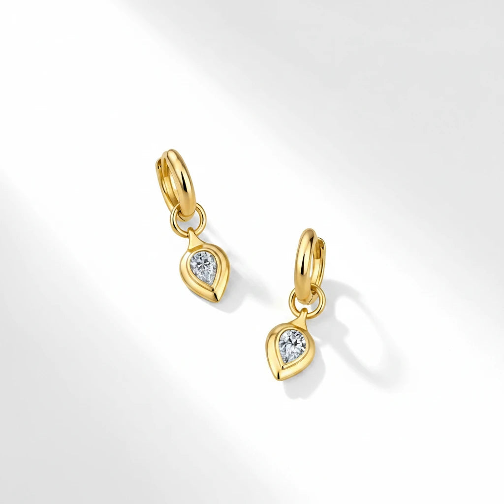 Gold earrings with teardrop-shaped gemstones on a light pink background