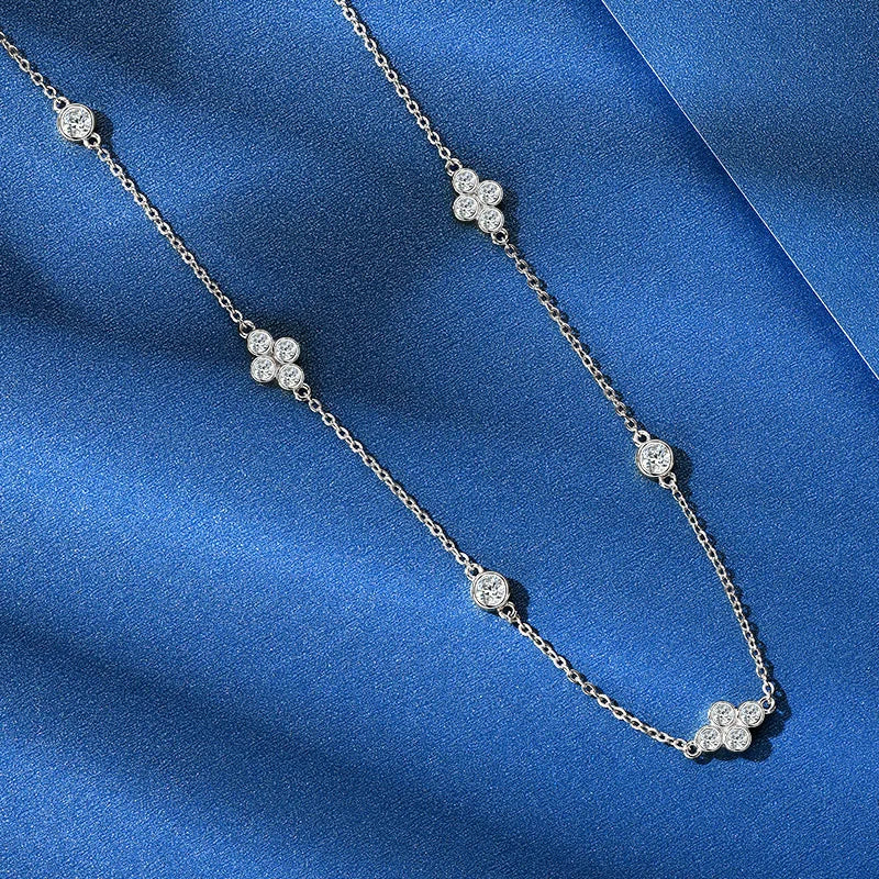 A silver-toned chain necklace with five small floral clover motifs set with clear stones, displayed on a textured blue fabric background.