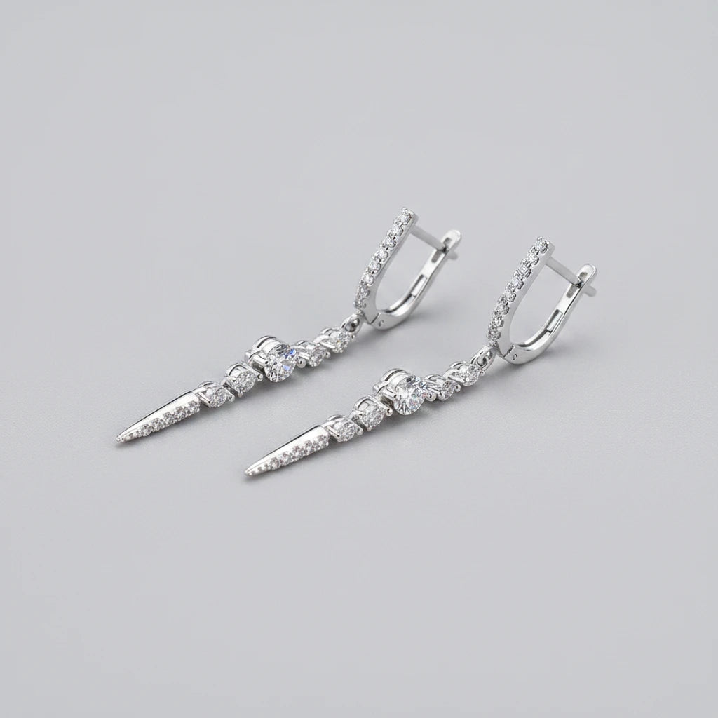 Pair of silver earrings with clear stones on a teal glittery background