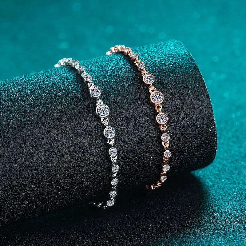 Two moissinite bracelets on a dark green textured surfacee 