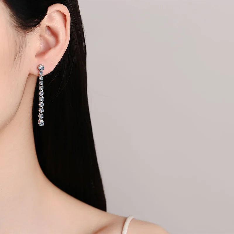 Close-up of a woman wearing a silver earring with a clear gemstone on a plain background