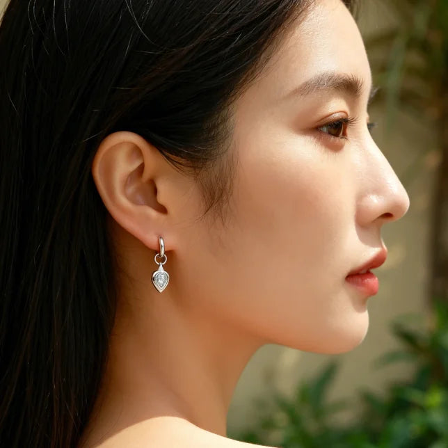 Close-up of a woman wearing a silver earring with a blurred green background