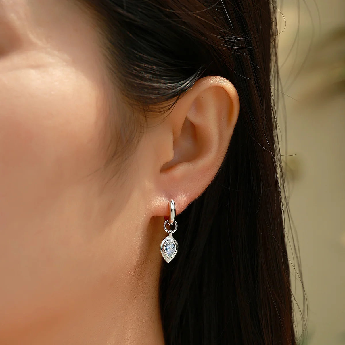 Close-up of a person wearing a silver earring with a clear gemstone.
