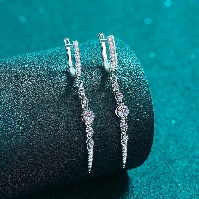 Silver earrings with clear stones on a dark teal surface
