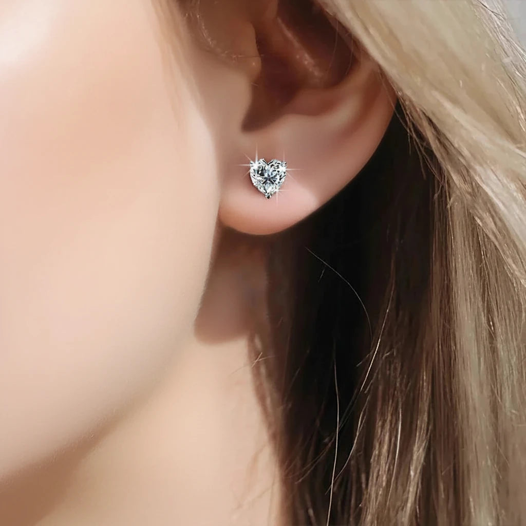 Heart-shaped silver earring worn by a person with blonde hair.