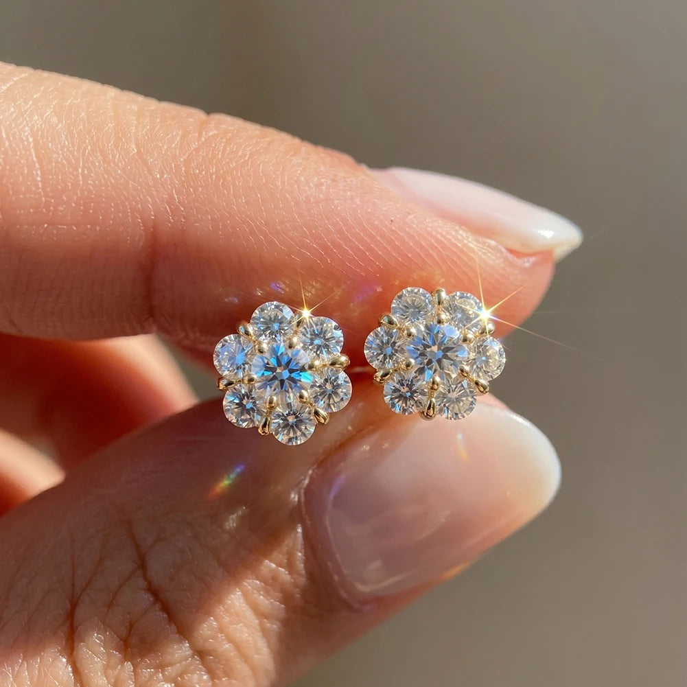 Flower-shaped diamond earrings held between fingers against a neutral background
