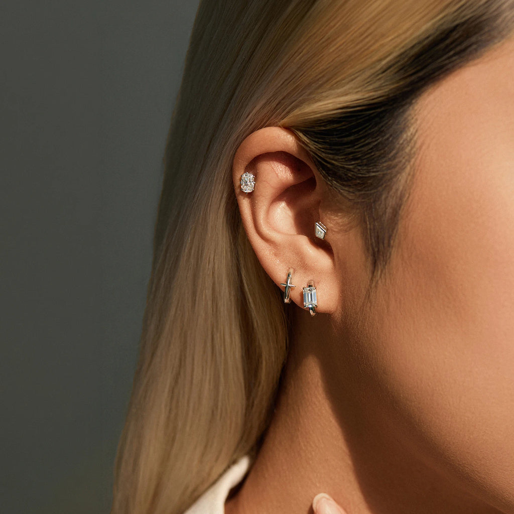 Close-up of a person wearing multiple diamond earrings against a neutral background