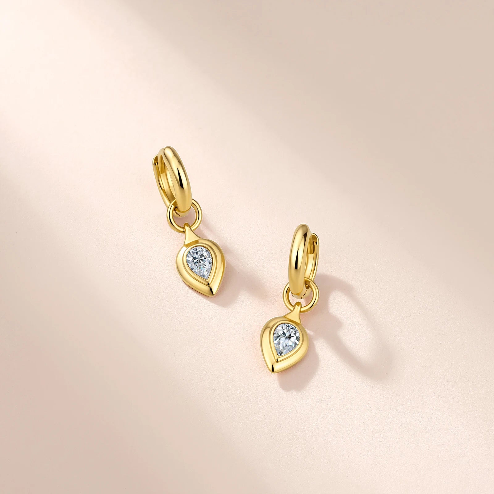 Gold earrings with teardrop-shaped gemstones on a light pink background