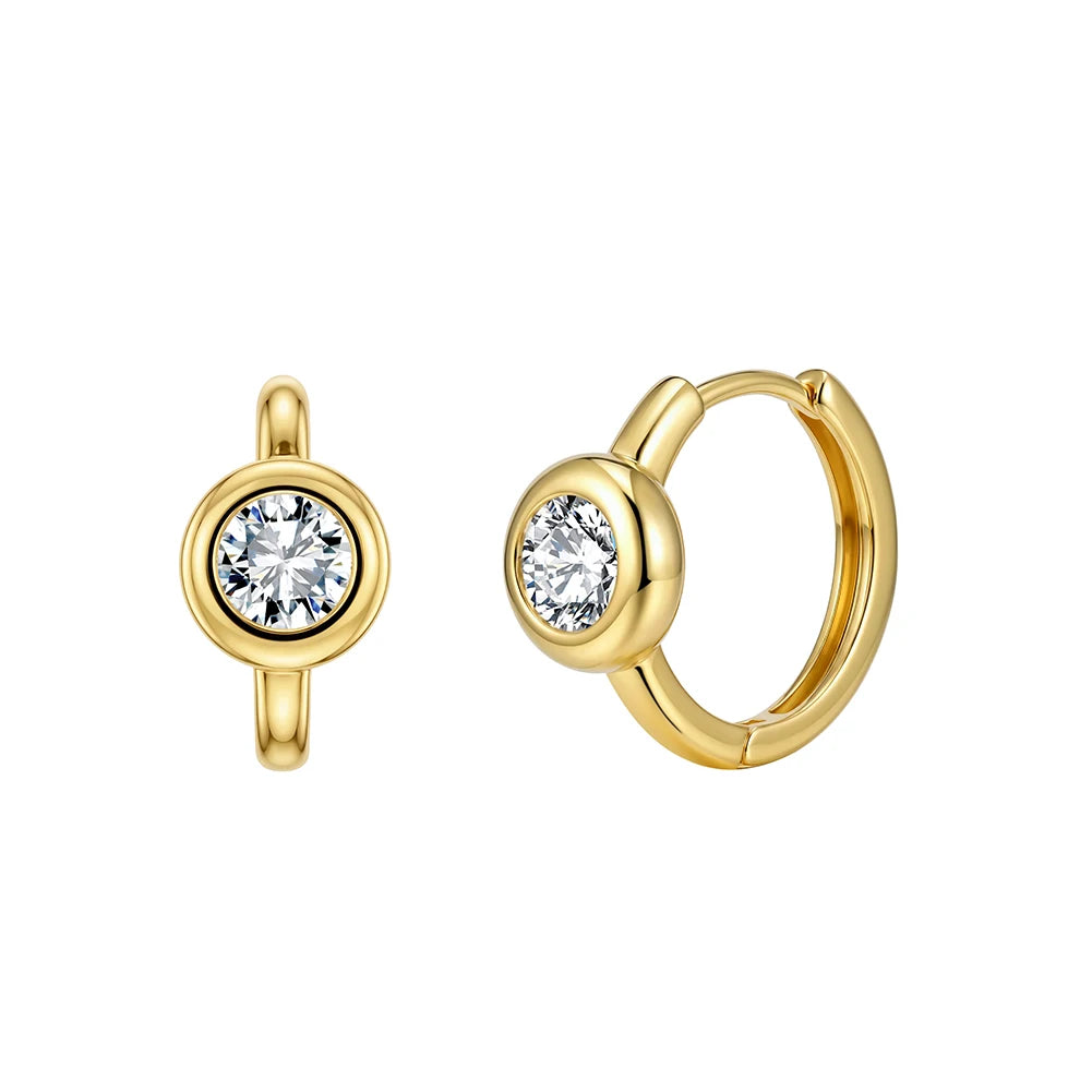 A pair of gold huggie hoop earrings with a bezel-set round clear gemstone, shown from front and side angles on a plain white background.