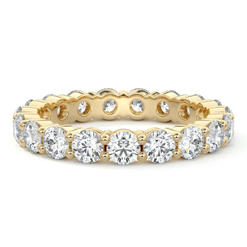 A yellow gold eternity ring featuring a row of round brilliant-cut diamonds and smaller round and oval diamonds, set against a clean white background.