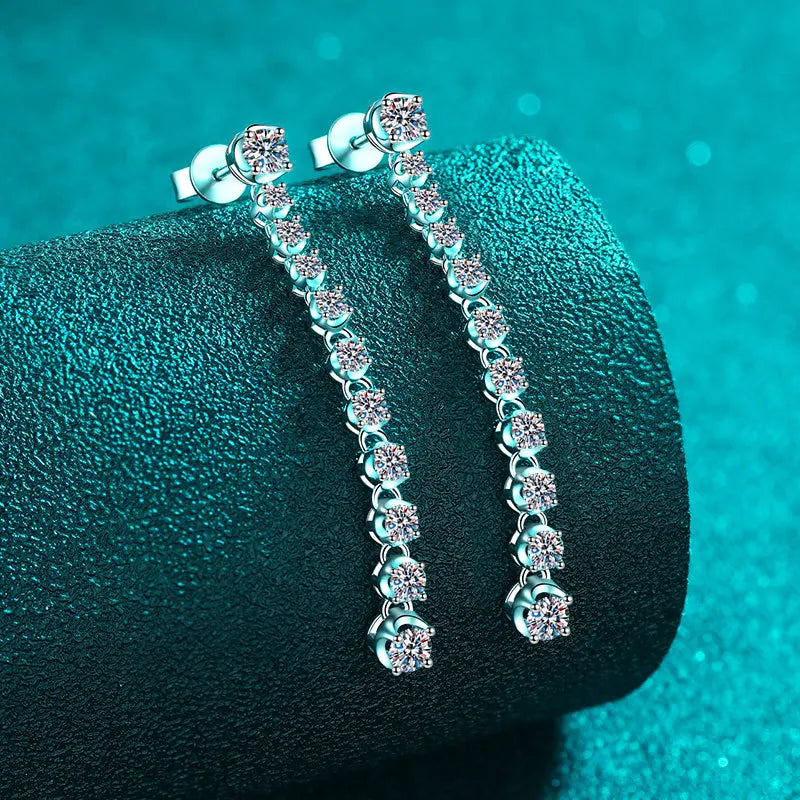 Pair of silver earrings with clear stones on a textured green surface