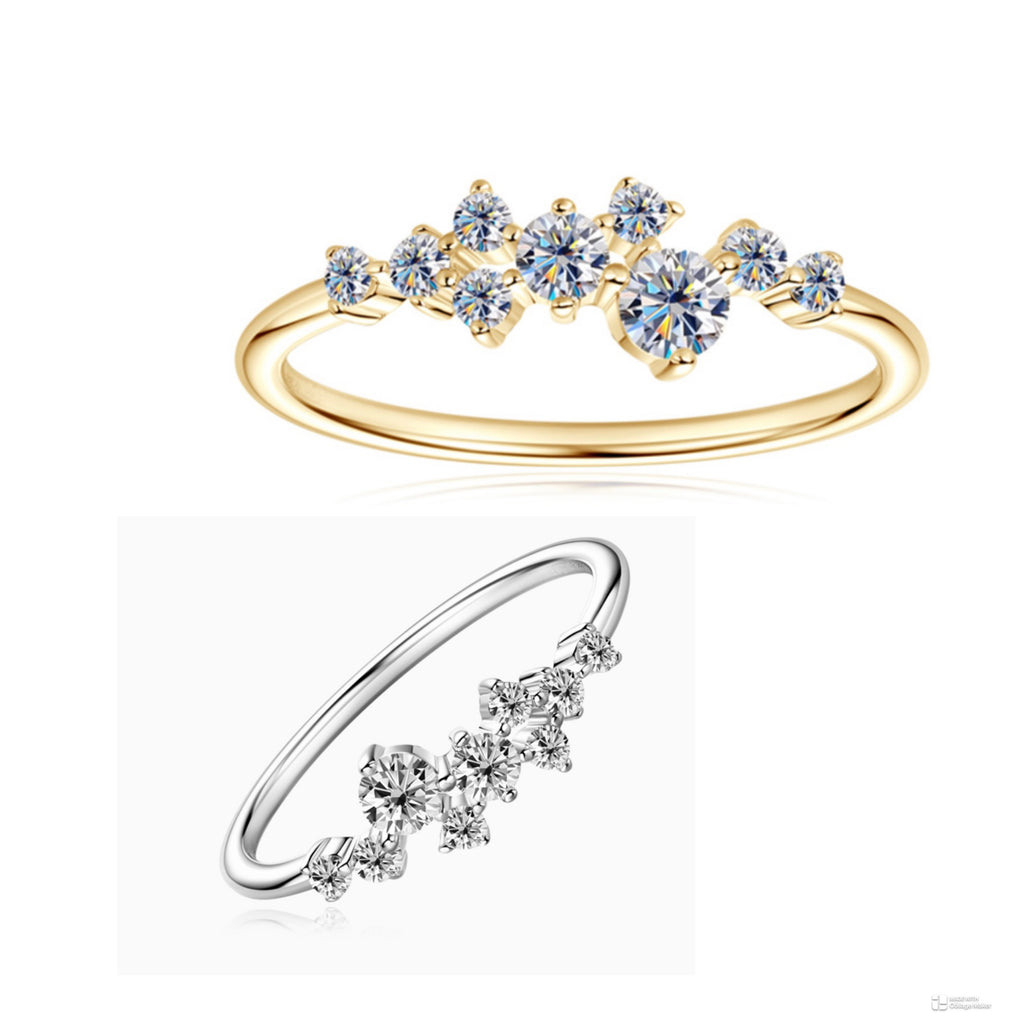 Two slim floral rings on a white background: a yellow gold ring with small blue gemstones at the top and a silver-toned ring with clear gemstones below.